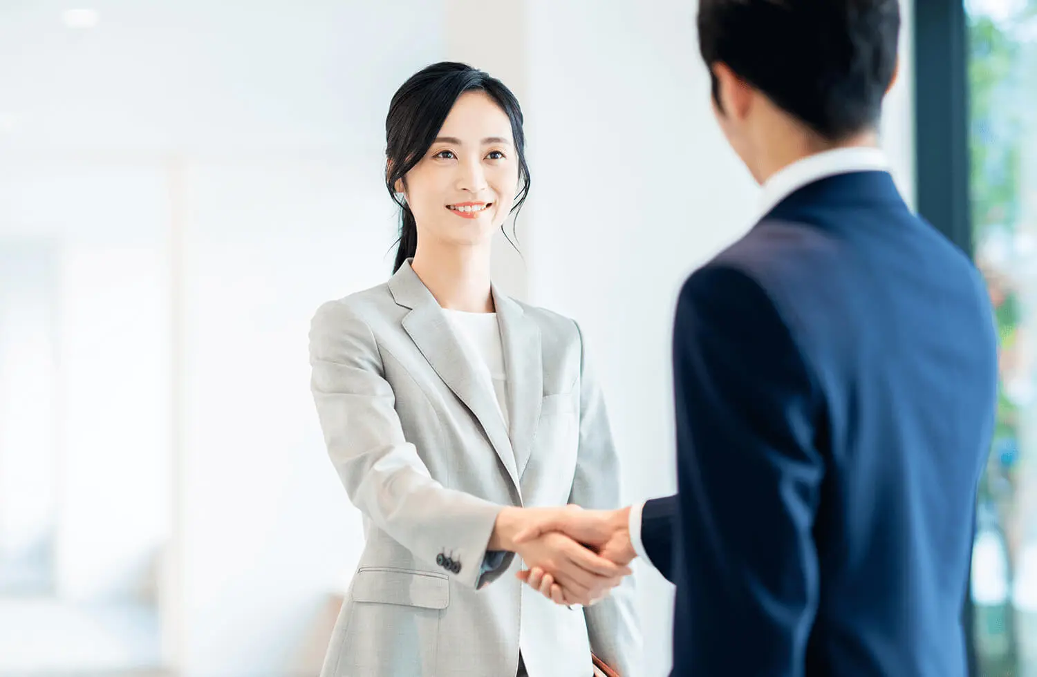 スーツを着た男女が笑顔で握手している様子