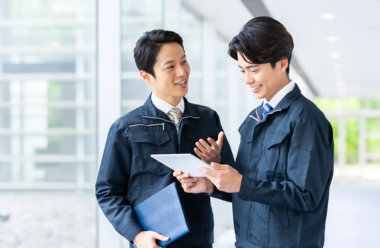 作業服を着た男性2人がタブレットを見ながら話している様子